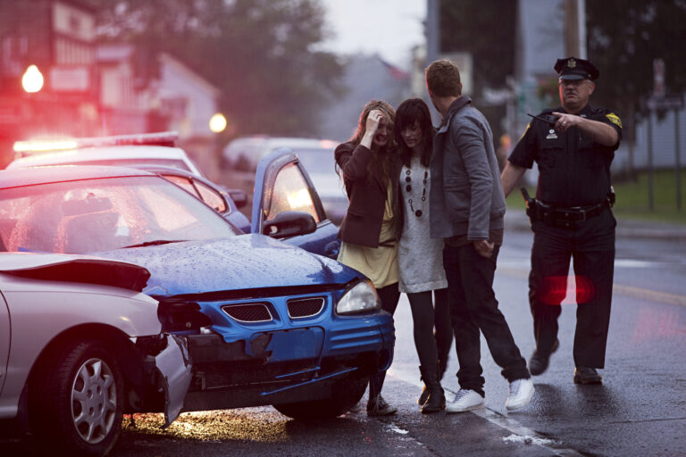 Woman comforted by man at car accident scene, police officer present.