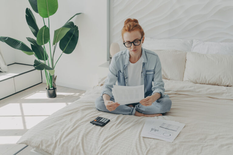 Woman reviewing home improvement documents and calculator on bed